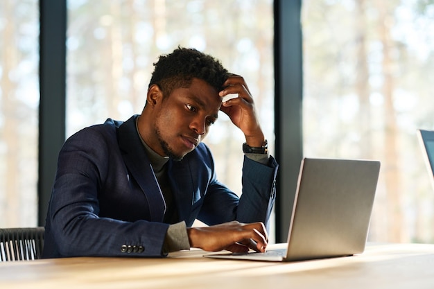 Young pensive or tense businessman sitting in front of laptop