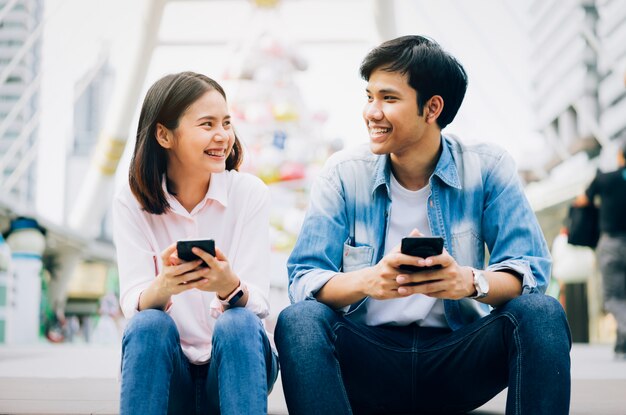 Young people are using smartphone and smiling while sitting on free time. 