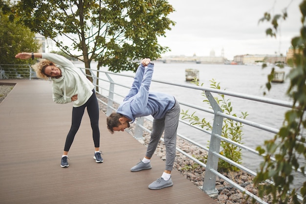 Young people doing stretching exercises during sports training in the park outdoors