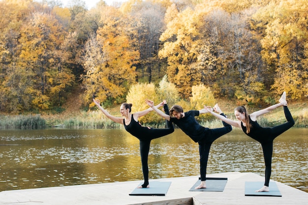 Young people doing yoga asana in nature near the lake