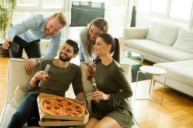 Young people eating pizza, drinking cider and taking selfie in the room