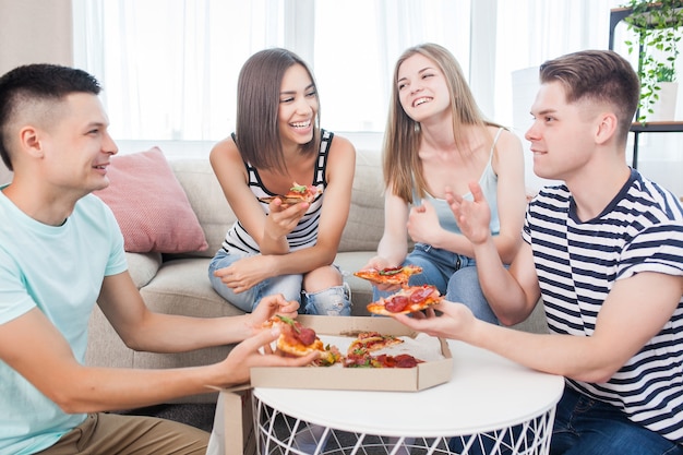 Young people eating pizza. Group of friends having lunch indoors. Funny friends together.