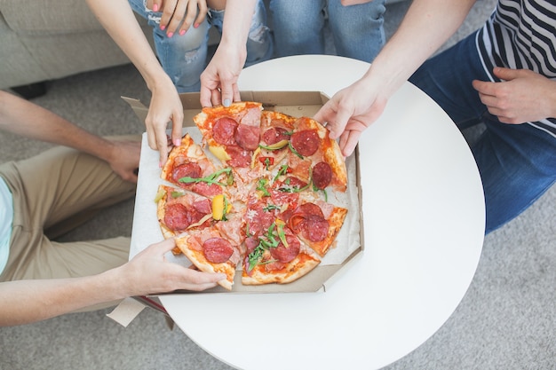 Young people eating pizza top view. Group of friends having lunch indoors. Funny friends together.