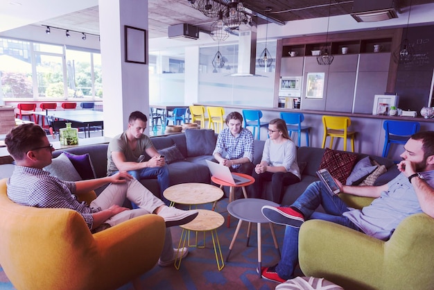 группа молодых людей в современном офисе проводит командные встречи и мозговой штурм, работая на ноутбуке и попивая кофе