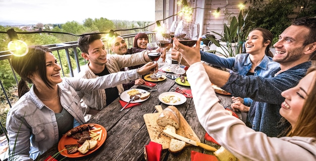 Young people having fun toasting red wine together at dinner party in outdoor villa