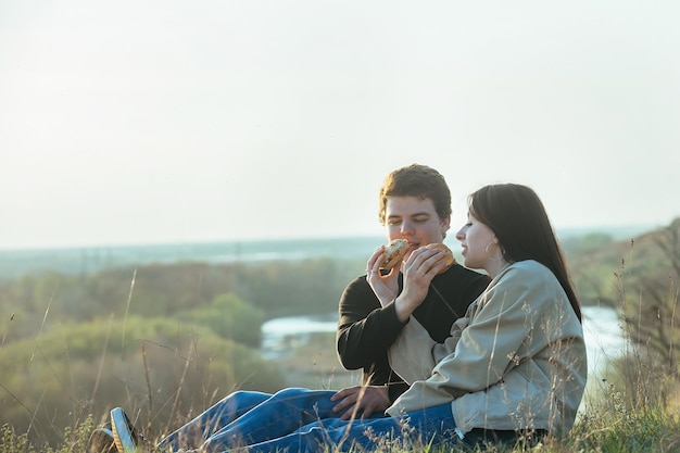 写真 恋をしている若者たちは自然の中でお互いにハンバーガーを食べさせる