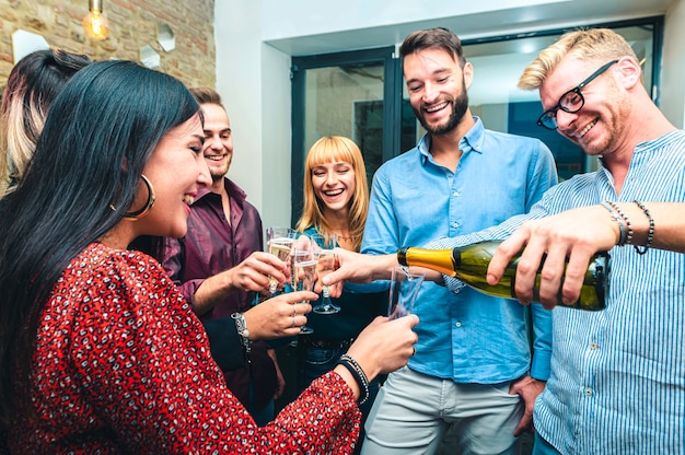 若い人たちはシャンパンを注いで誕生日を祝う-若い同僚のグループは成功のために祝って乾杯する-選択的な焦点