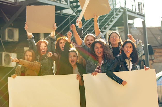 young people protesting of women's rights and equality on the street. caucasian women have meeting about problem in workplace, male pressure, domestic abuse, harassment. copyspace. holding posters.