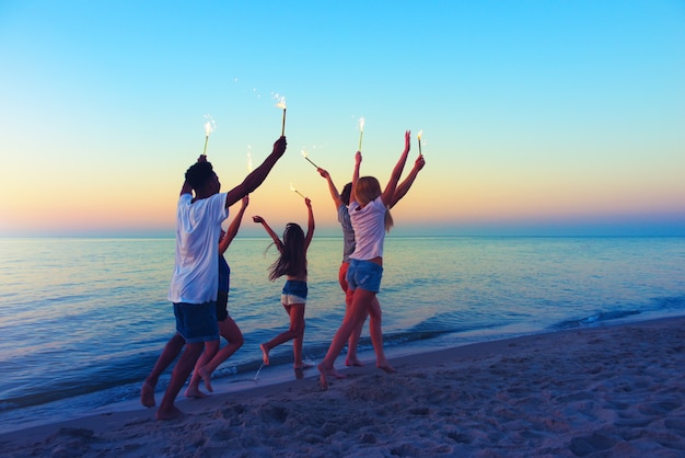 Young people run on the beach with sparkling candles in the hands