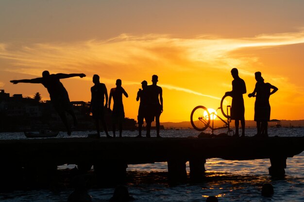 Young people and silhouettes are seen together during sunset having fun on top of the Crush bridge in the city of Salvador Bahia