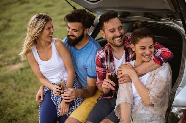 Young people sitting in the car trank during trip in the nature