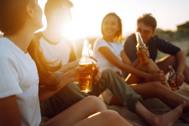 Young people sitting together at beach drinking beer Group of friends cheers with beers at the beach