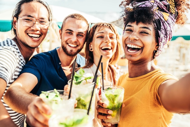 Giovani che tostano drink mojito al cocktail bar sulla spiaggia amici multirazziali felici che si divertono