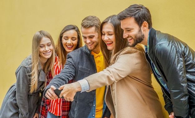 Young people using smartphones group of social media co workers\
having fun and takeing a selfie obsessed with online and shareing\
lifestyle moments technology concept