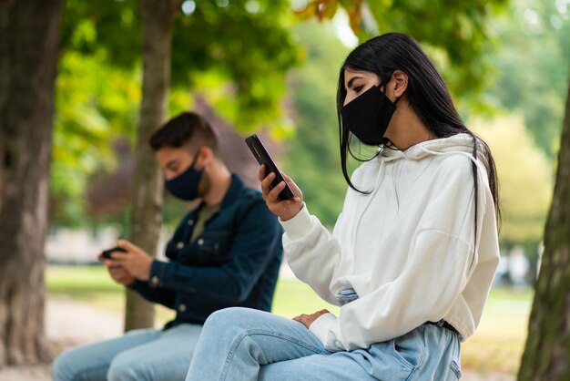 Photo young people using their smartphone while wearing a mask outdoor coronavirus and social distancing