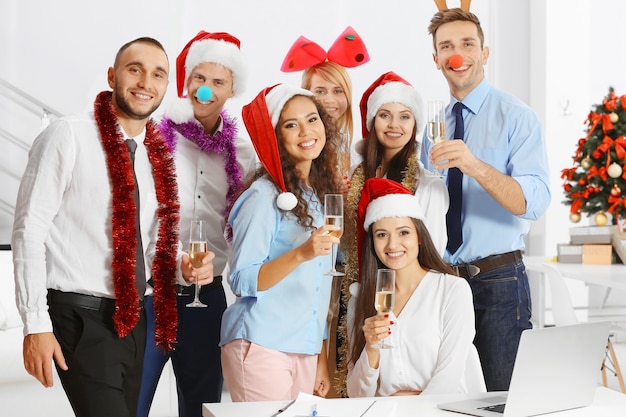 Young people with glasses of champagne celebrating Christmas at corporate party in office