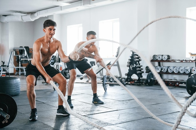 Young people with sportive body shapes doing crossfit by using knots