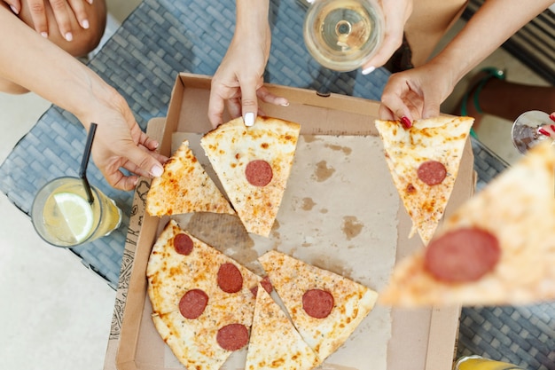 Young people womens taking slices of hot tasty pizza from cardboard box top view