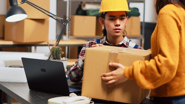 Young person doing warehouse inventory with pc, organizing products in packages on racks. Male employee working in storage room to plan order shipment, merchandise distribution.