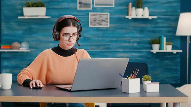 Young person talking on online videoconference with headphones,\
using remote video call meeting to attend school class. female\
student working with headset on computer at desk.