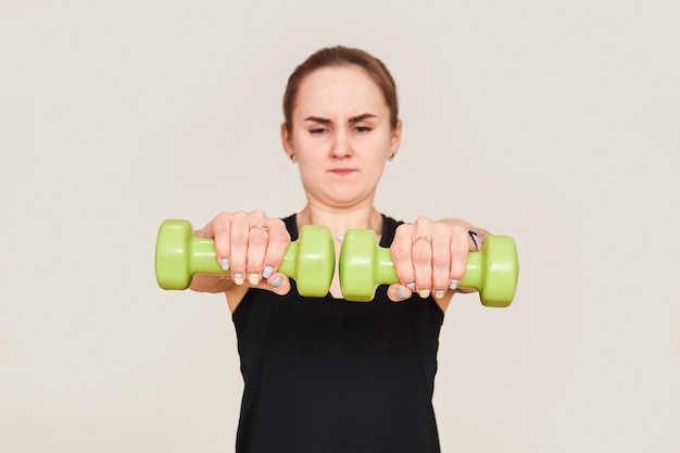 Young petite woman performs exercises with dumbbells