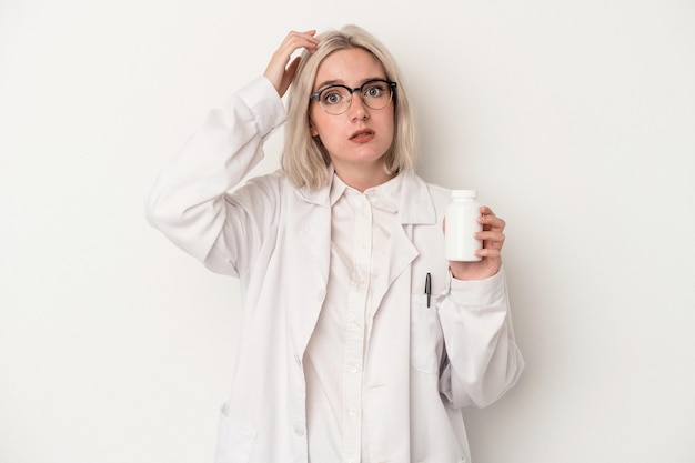 Young pharmacist woman holding pills isolated on white background being shocked she has remembered important meeting