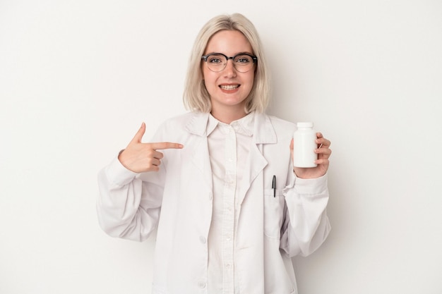 Young pharmacist woman holding pills isolated on white background person pointing by hand to a shirt copy space proud and confident