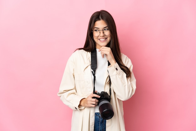 Молодой фотограф бразильская девушка изолирована на розовой стене, глядя в сторону и улыбаясь