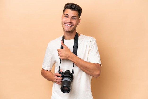 Young photographer caucasian man isolated on beige background giving a thumbs up gesture