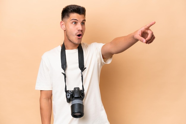 Young photographer caucasian man isolated on beige background pointing away