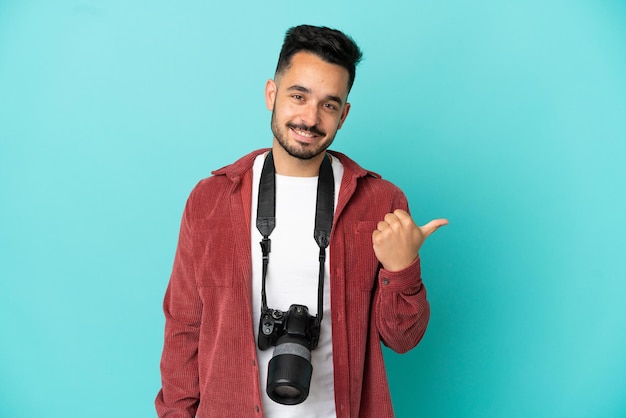 Giovane fotografo caucasico uomo isolato su sfondo blu che punta al lato per presentare un prodotto