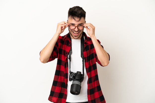 Foto giovane fotografo caucasico uomo isolato su sfondo bianco con gli occhiali e sorpreso