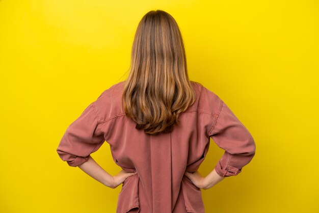 Young photographer caucasian woman isolated on yellow background in back position