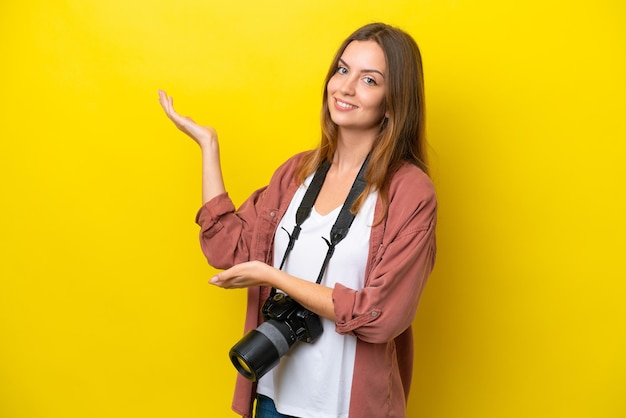 Young photographer caucasian woman isolated on yellow background extending hands to the side for inviting to come