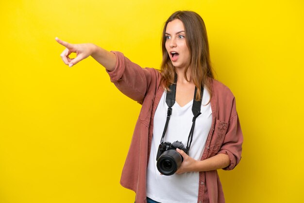 Young photographer caucasian woman isolated on yellow background pointing away