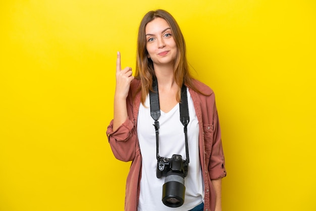 人差し指で指している黄色の背景に分離された若い写真家白人女性素晴らしいアイデア