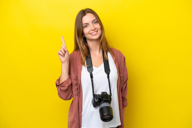 Young photographer caucasian woman isolated on yellow background showing and lifting a finger in sign of the best