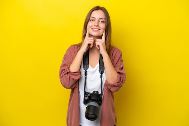 幸せで楽しい表情で笑顔の黄色の背景に分離された若い写真家白人女性