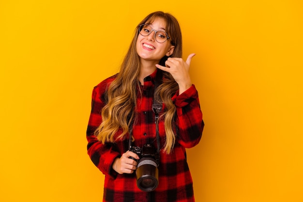 Young photographer caucasian woman on yellow showing a mobile phone call gesture with fingers.