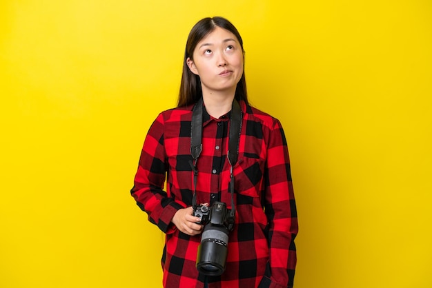 Giovane fotografo donna cinese isolata su sfondo giallo e alzando lo sguardo