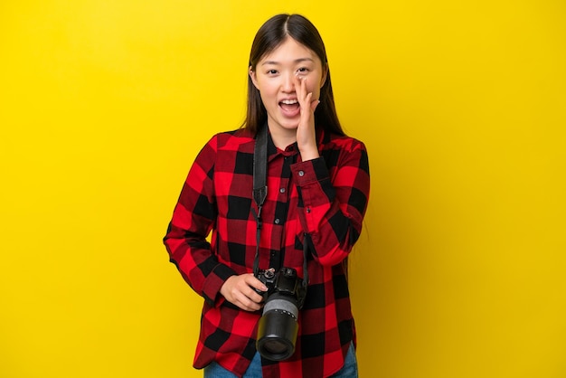 Young photographer Chinese woman isolated on yellow background shouting with mouth wide open