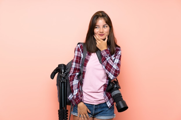 アイデアを考えて孤立したピンクの壁の上の若い写真家の女の子