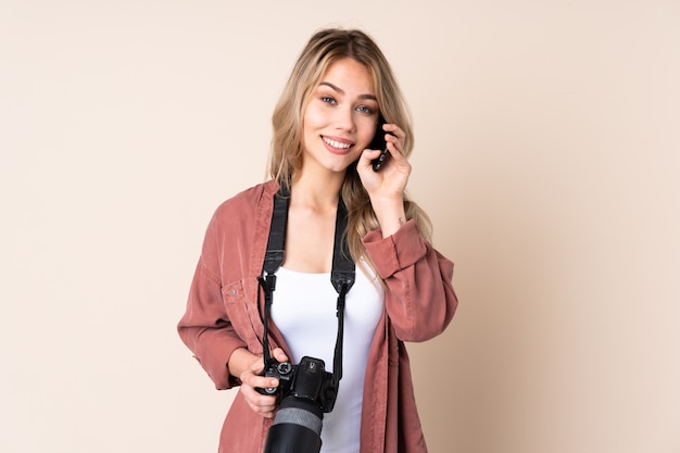 Ragazza del giovane fotografo sopra la parete isolata che mantiene una conversazione con il telefono cellulare con qualcuno