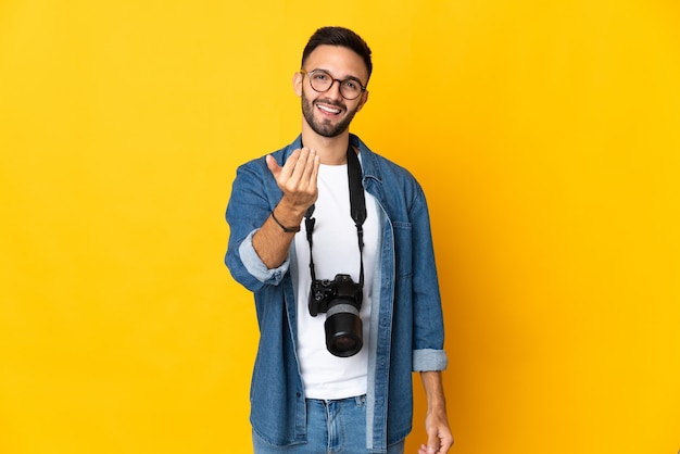 Young photographer girl isolated on yellow background inviting to come