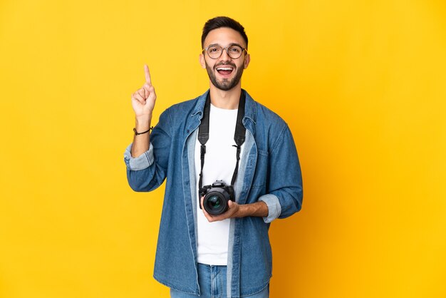 素晴らしいアイデアを指している黄色の壁に分離された若い写真家の女の子