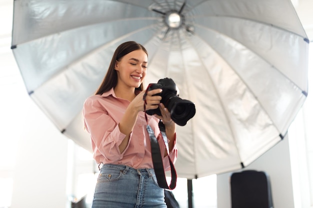 Young photographer lady working with professional camera in front of reflective umbrella in modern