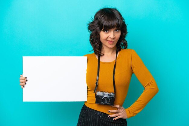 Молодой фотограф латиноамериканка изолирована на синем фоне с пустым плакатом