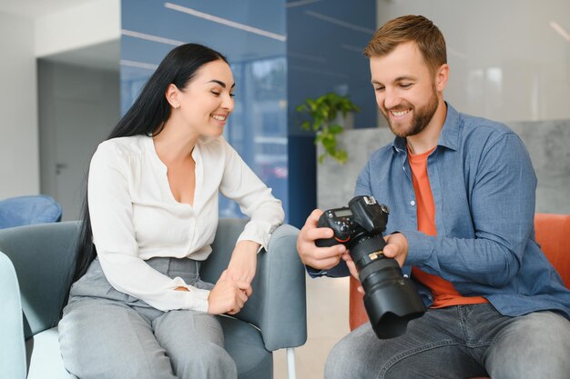 Young photographer man in blue shirt watching photo with client
woman after photo session and smiling and looking at each
other