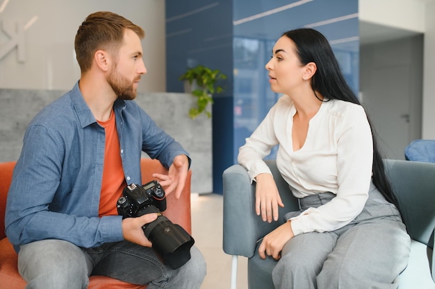 Giovane fotografo uomo in camicia blu che guarda la foto con la donna del cliente dopo la sessione fotografica e si sorride e si guarda l'un l'altro