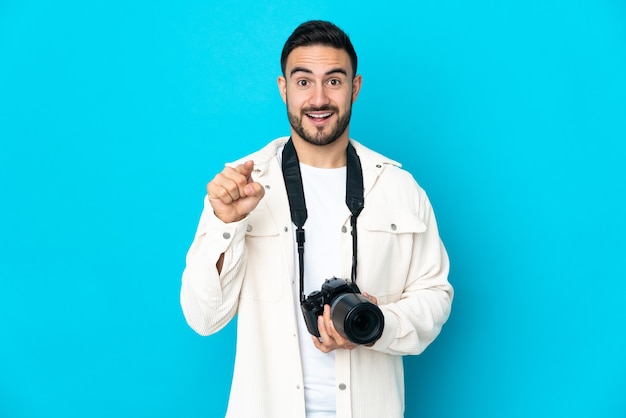 Young photographer man isolated on blue wall surprised and pointing front